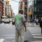 Man standing on the corner of a busy intersection wearing baggy Denim pants and a hat waiting for the walk signal